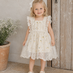 Young girl in a white lace dress standing in front of a wooden door.